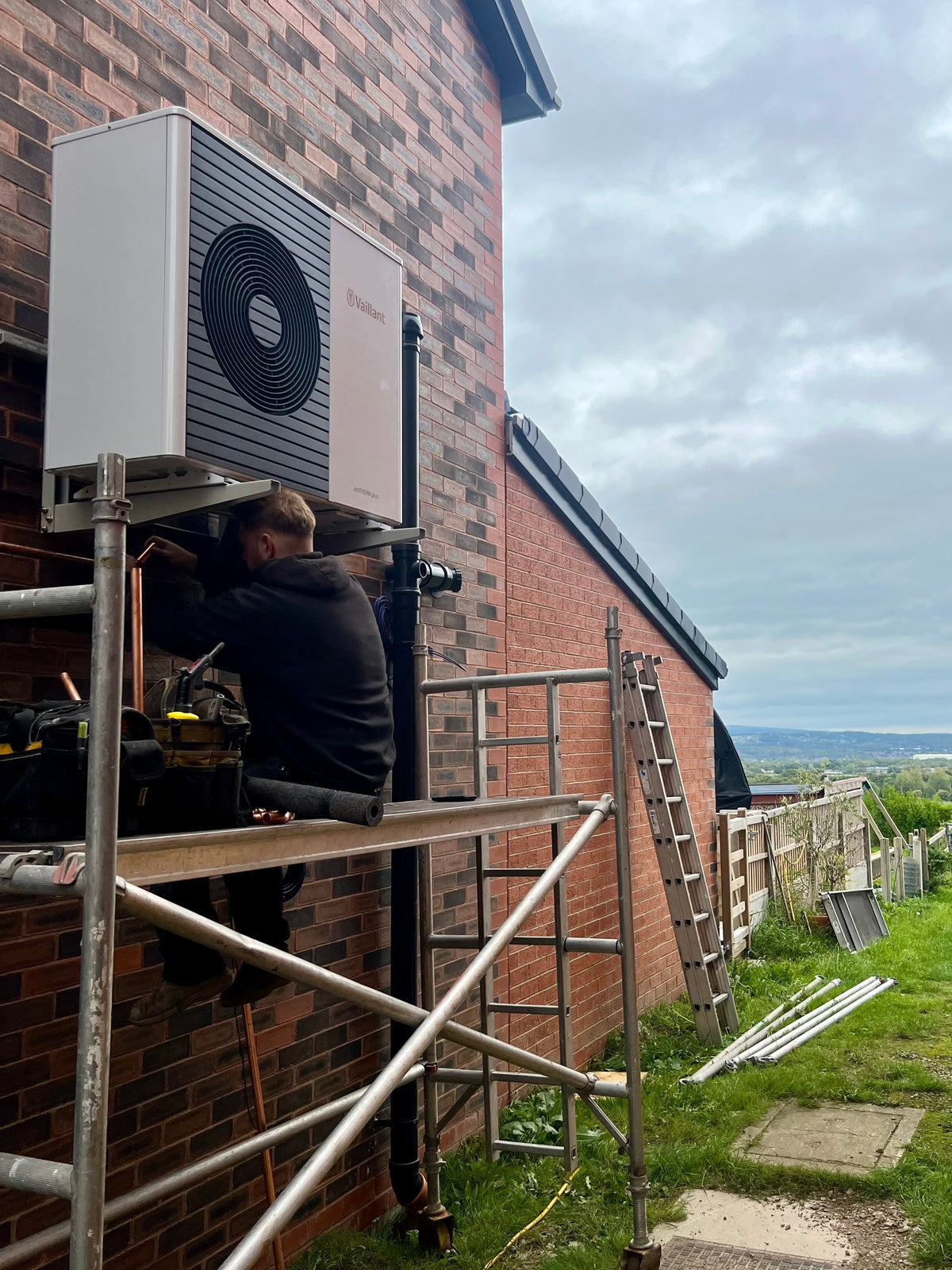 Person installing an air conditioning unit on a brick wall with scaffolding.